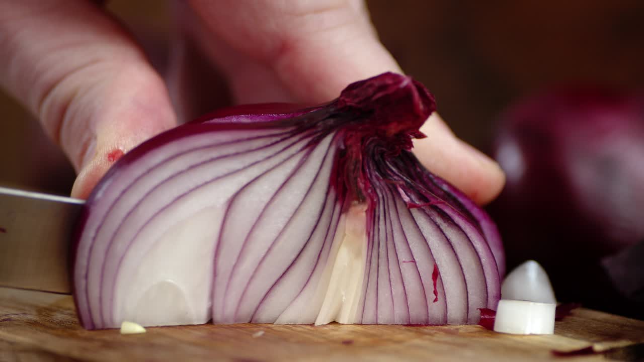 The hand of a man with a knife cut the red onion into pieces.