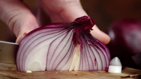 the hand of a man with a knife cut the red onion into pieces.