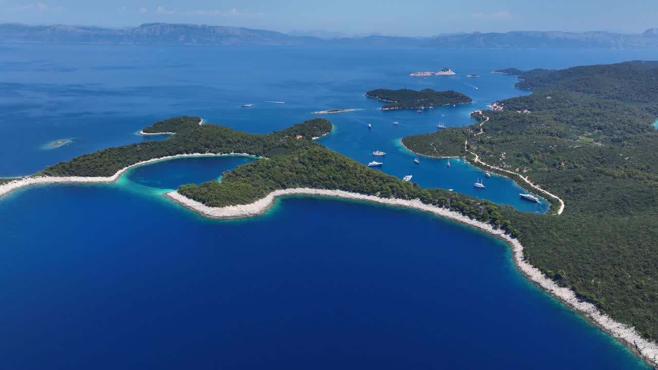 Bird's eye drone view of forested coastline, coves, anchored yachts and rugged shorelines stretching into the Adriatic Sea, Mljet, Croatia