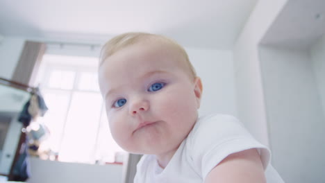 baby boy sitting on parents bed reaching out towards camera