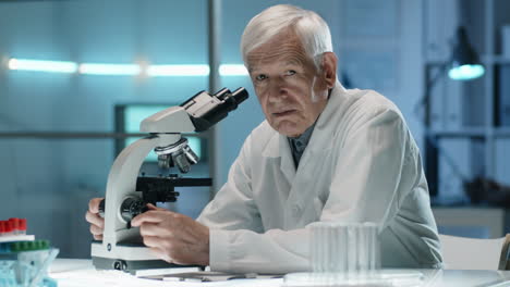 científico sénior trabajando con el microscopio y posando para la cámara