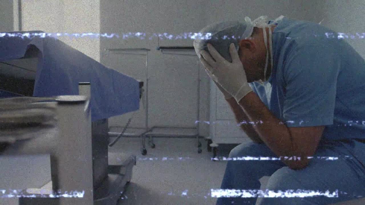Chirurgo uomo seduto a un tavolo drappeggiato che osserva un vassoio e si infila i guanti, tra linee statiche che mostrano stress.