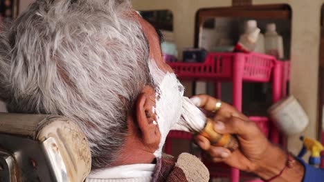 el peluquero aplicó espuma de afeitar con un hisopo en la cara de un anciano, un hombre afeitándose en una barbería