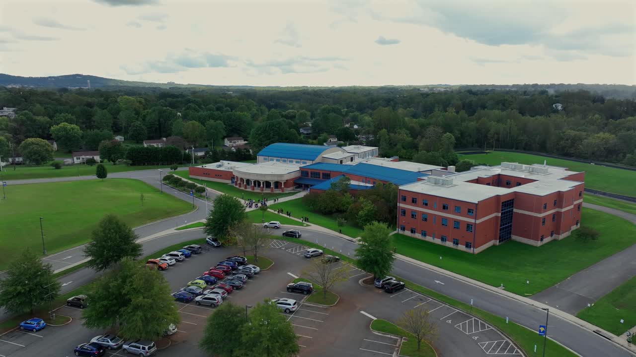Aerial approaching shot of Sandusky elementary school in Lynchburg, Virginia. Cloudy day in American suburb district with green trees in autumn. Parking cars and leaving pupils after school.