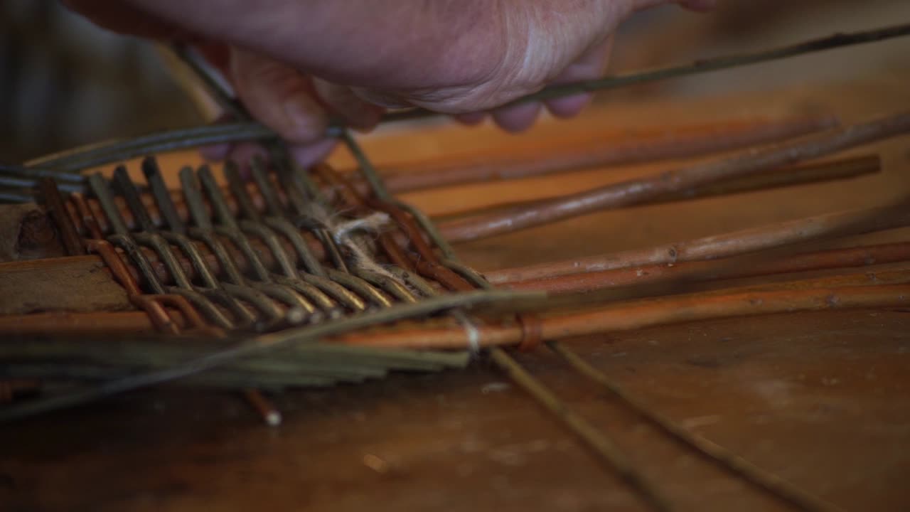 Extreme close-up of a basketmaker's hands weaving together the wooden rods of a welsh basket