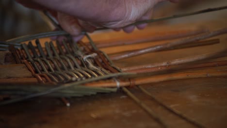 primer plano extremo de las manos de un cestero tejiendo las varillas de madera de una canasta galesa