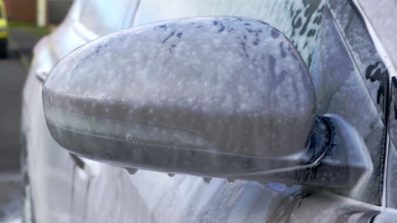 Orbiting shot of SUV mirror cover in shampoo snow foam and bubbles - close up orbit