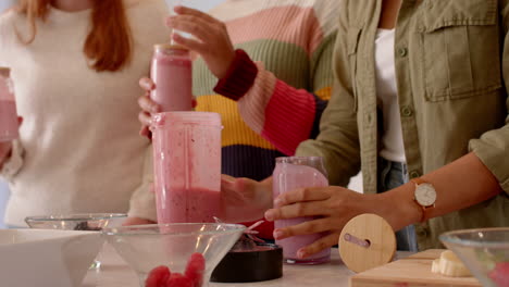 making smoothies, female friends holding glasses and blender, enjoying time together in kitchen