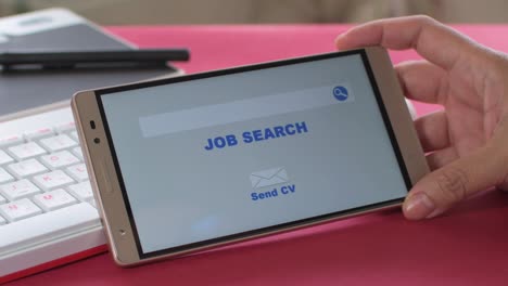 online job search, woman's hands holding a mobile in which an employment website appears. work desk with keyboard in the background.
