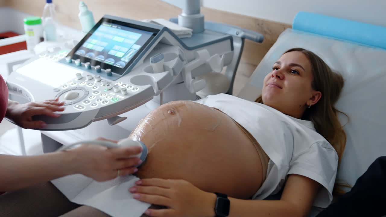 Beautiful Caucasian pregnant lady lies having ultrasound check up. Doctor's examination of pregnancy on last stages.