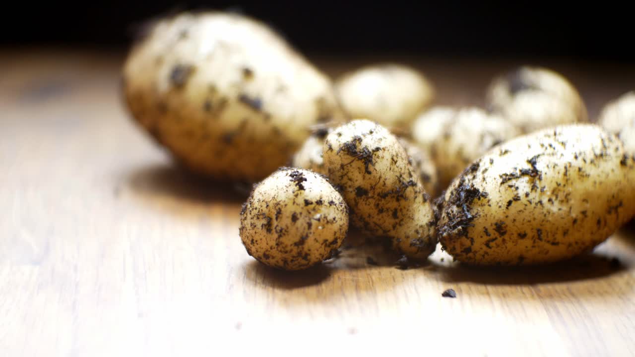 Patate biologiche casalinghe con messa a fuoco ridotta, ancora sporche di terra su una superficie di legno in cucina.