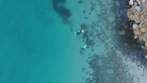 Arial-view-of-three-scuba-divers-swimming-underwater-following-each-other-using-waterproof-torches