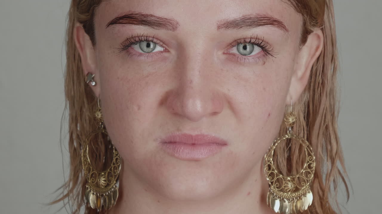 Ethereal Blonde Muse: Wet Waves and Ornate Gold Earrings in Thoughtful Gaze. This captivating close-up portrait features a young woman with sun-kissed blonde hair, damp and tousled from a recent rinse