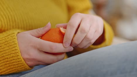 mujer joven pelando naranja o mandarina blanca sentada, acogedor paisaje doméstico