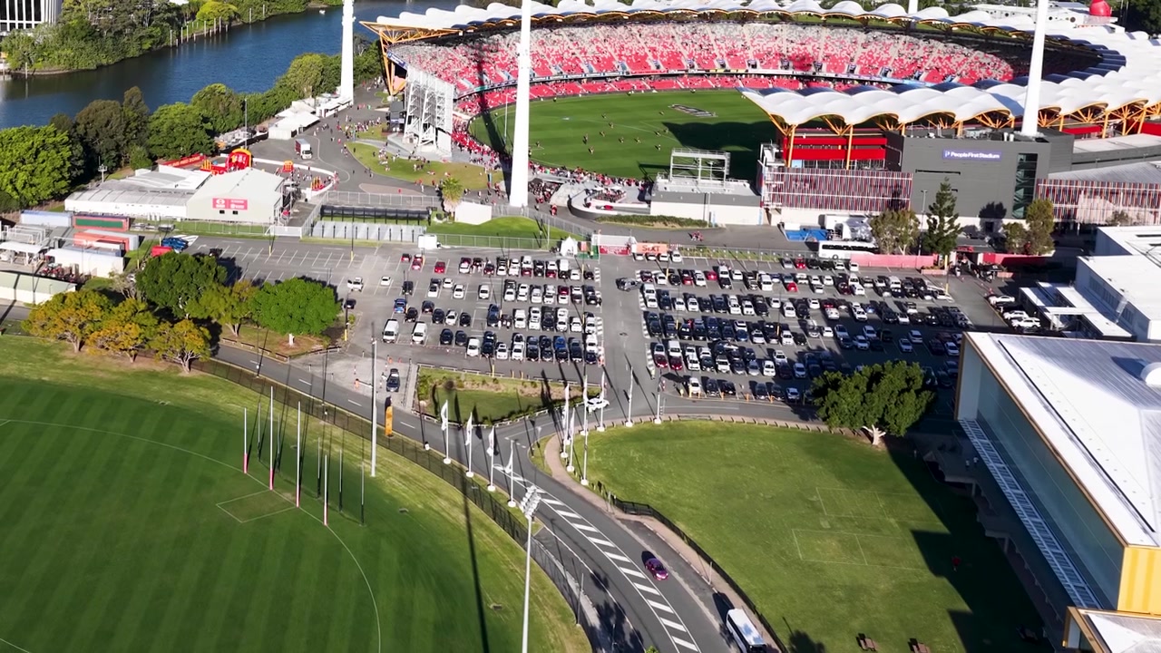 High angle drone shot captures a modern sports arena, parking lot, and green fields.