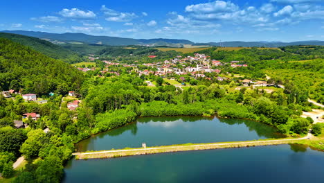 calm lakeside village scene. lush green hills surround a quaint village nestled by a tranquil lake under a bright blue sky