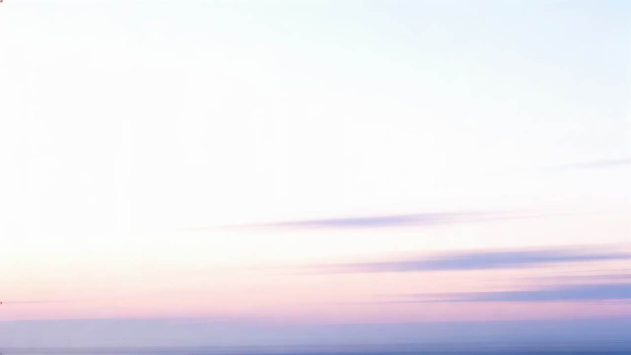 Drifting elongated cloud bands crossing wide pastel sky as sunrise brightening horizon, sea glowing