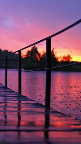 heavy rain with small lightning over the river. long footbridge in the river during the rain in the evening in summer. beautiful natural background at sunset with rainy drops outdoors. vertical video