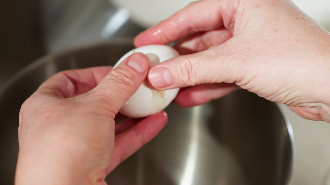 Close up of person delicately cracking white egg over stainless steel bowl, carefully separating shell to pour egg white without letting yolk fall into bow