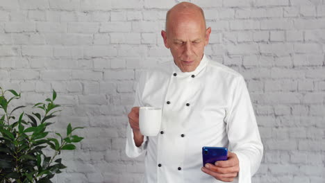 un jefe de cocina senior maduro se toma un descanso de la cocina y envía mensajes de texto a su teléfono mientras bebe café
