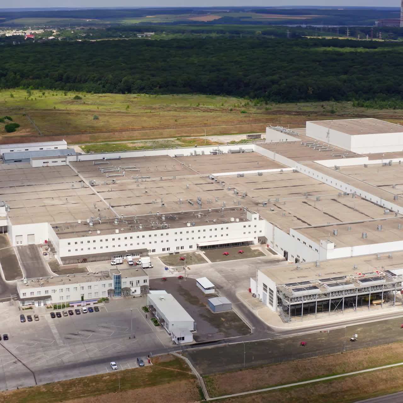 Industrial zone in the countryside. Huge commercial plant on field in summer nature. Modern factory among green environment. Aerial view