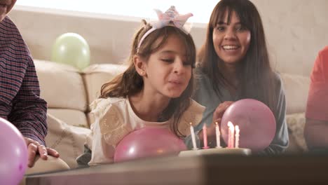 girl blowing out the candles on her birthday cake sitting on a sofa