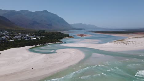 Stunning-coastal-lagoon-estuary-system-as-seen-from-above-with-waves-entering-the-open-lagoon-mouth-and-mountains-in-the-distance