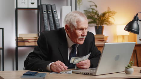 rich grandfather businessman working on laptop counting money cash calculate profit at home office