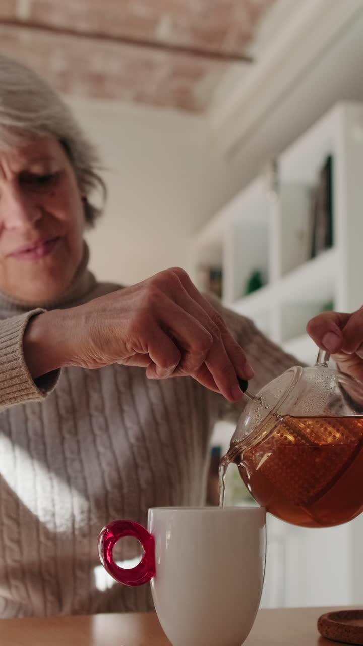 Donna anziana che versa tè caldo da una teiera in una tazza
