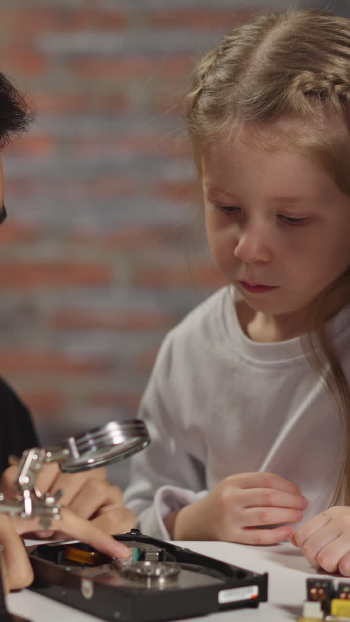 Asian male engineer shows open hard disk drive to curious little student near working African-American colleague at table with devices closeup