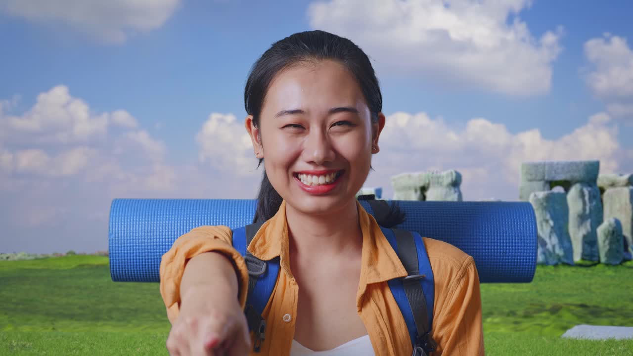 Close Up Of Asian Female Hiker With Mountaineering Backpack Smiling, Touching Her Chest, And Pointing To Camera While Traveling In Stonehenge