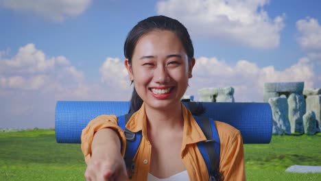 close up of asian female hiker with mountaineering backpack smiling, touching her chest, and pointing to camera while traveling in stonehenge