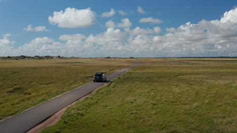 Forwards-tracking-of-car-on-tarmac-pathway-in-countryside.-Flat-grass-landscape-and-blue-sky-with-clouds.-Denmark
