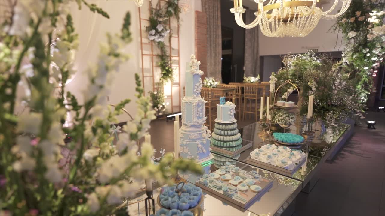 Lateral tracking shot from floral foreground revealing blue dessert table setup