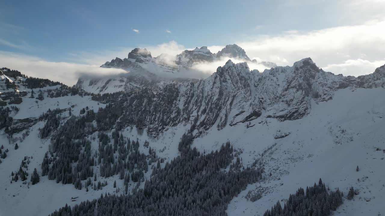 Cresta frastagliata esposta con cime montuose più alte coperte di neve e nuvole che svettano sopra una foresta di pini