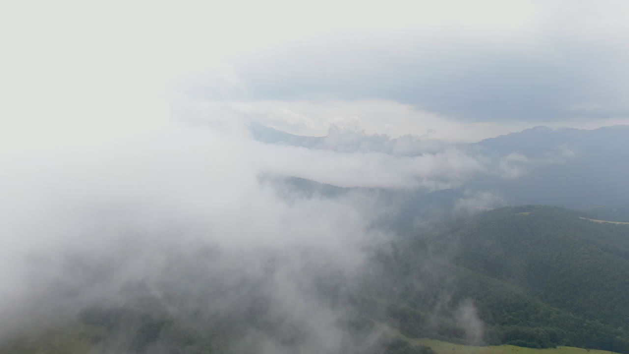 A view of a mountain range partially covered by clouds The sky is overcast and the landscape is green with hints of sunlight breaking through