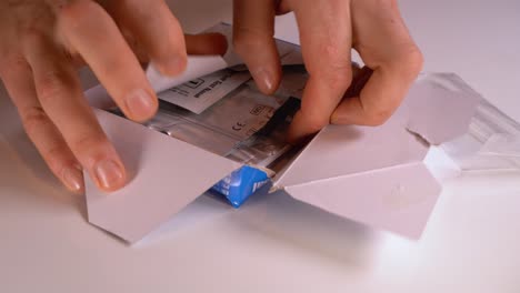 closeup of hands opening antigen test kit and laying content on white surface table close to camera - static closeup