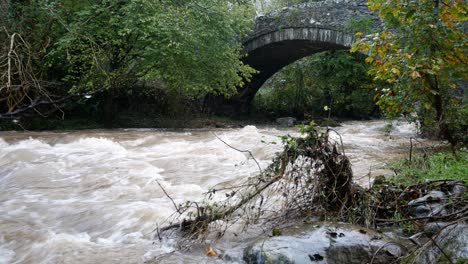 rapid flowing river water cascades under idyllic rural arched stone bridge wilderness dolly right slow