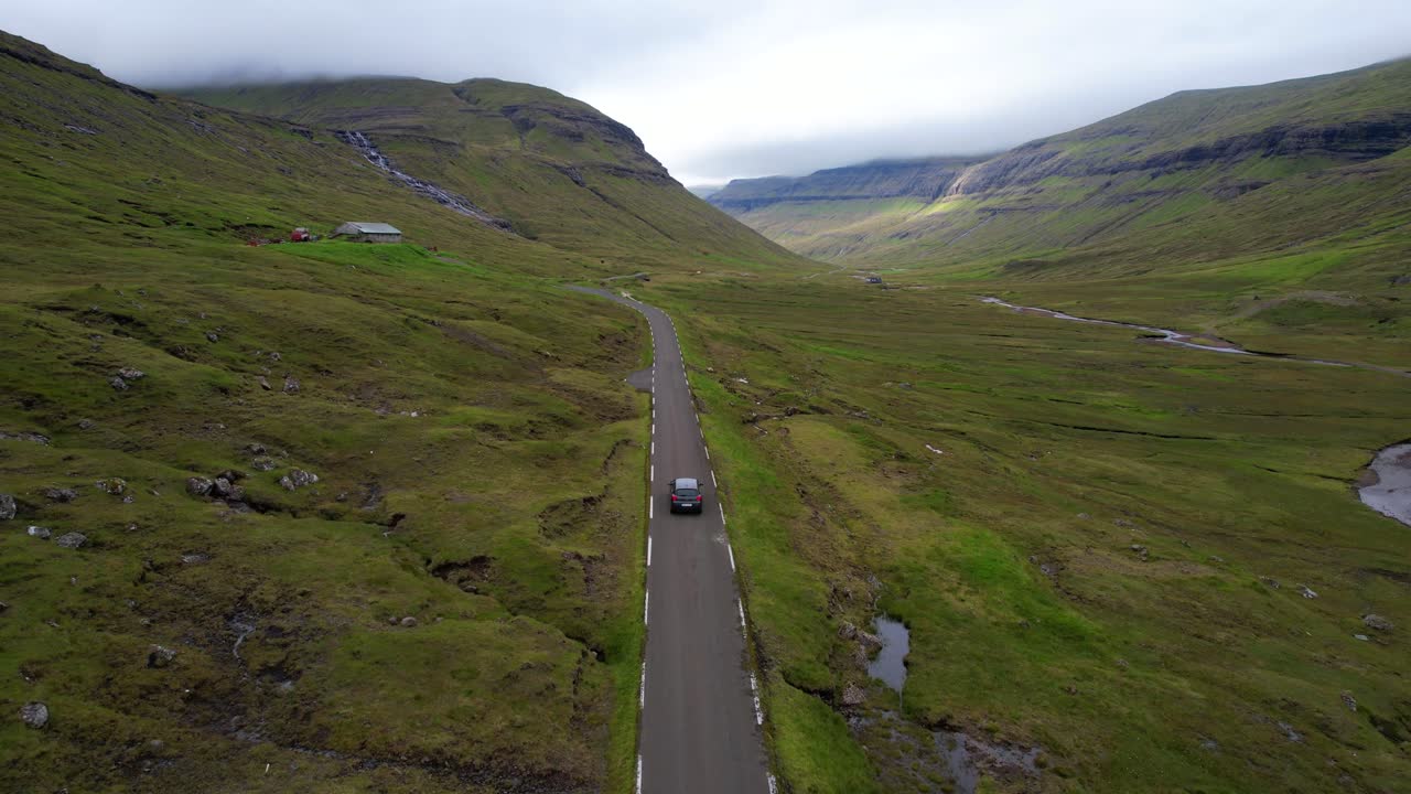 페로 섬의 시골 도로에서 자동차가 운전하는 것을 따라가는 화려한 항공 사진, 서사시적인 풍경