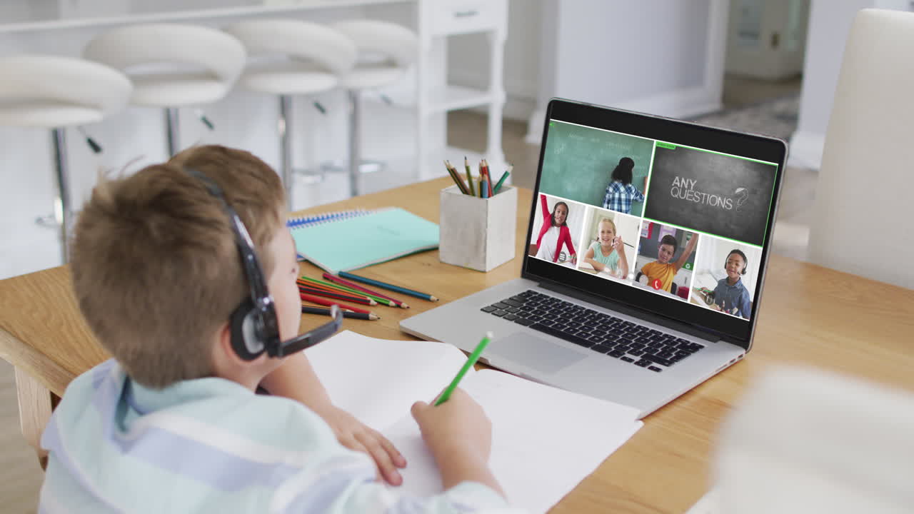 Schoolboy using laptop for online lesson at home, with diverse teacher and class on screen