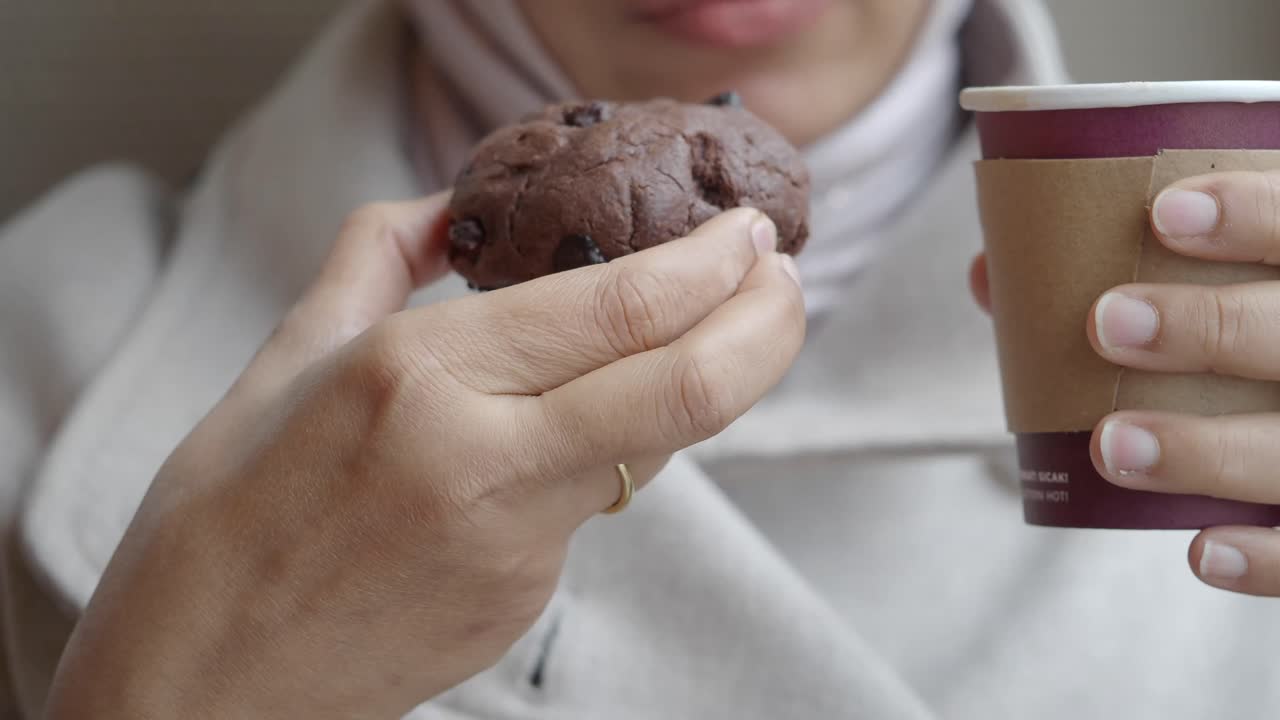 Primo piano di mani che tengono un muffin al cioccolato e una tazza di caffè