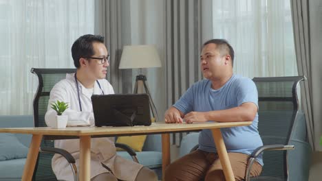 asian male doctor with a fat male patient in clinic, sitting at desk, discussing about the results of medical check up on a tablet, giving bad news, encouraging a patient