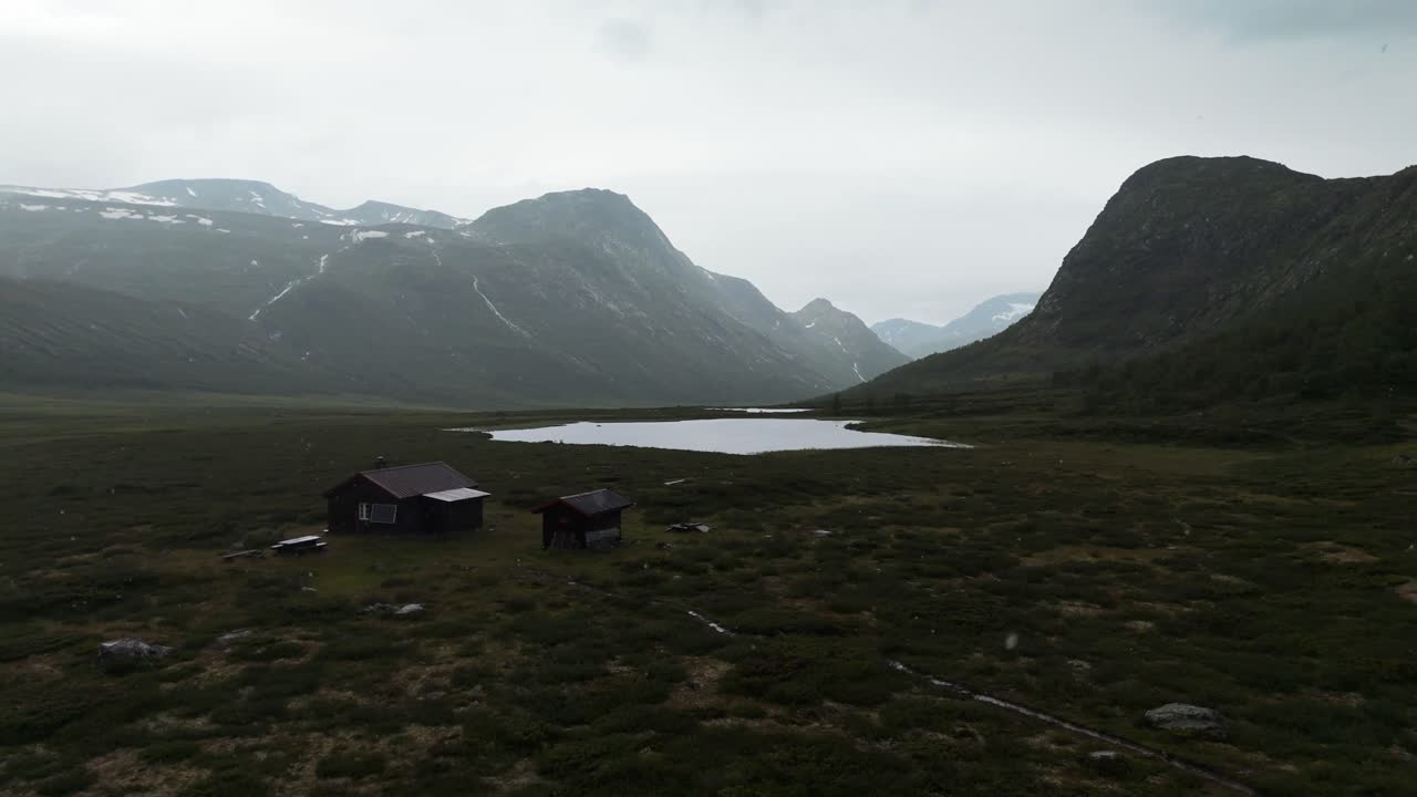 Aerial landscape showcasing a winding river on a valley floor surrounded by dark rain-soaked mountains, creating a moody atmosphere.