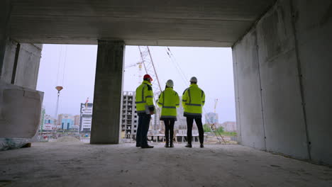 el capataz, la arquitecta femenina y el inspector de construcción están examinando el sitio de construcción de vista trasera