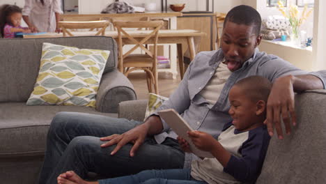 father and son sit on sofa in lounge using digital tablet