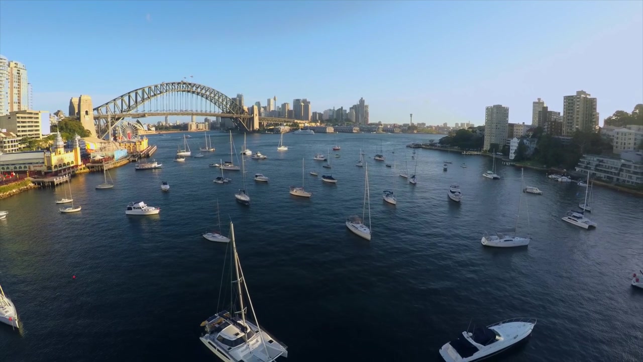 Ripresa drone che si allontana dal Sydney Harbour Bridge sopra barche e yacht nel tardo pomeriggio o prima serata sul porto di Sydney