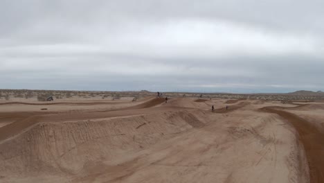 motorcycles taking long jumps along a motocross racetrack in the mojave desert - aerial view