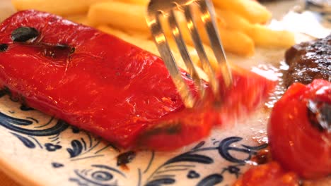 close up of a grilled red pepper with french fries and meat on a plate