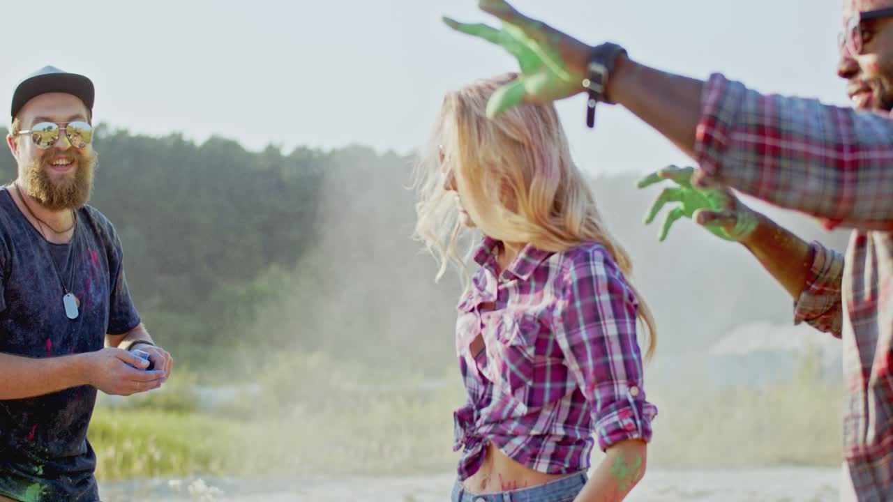 jóvenes multiétnicos y alegres chicos y chicas divirtiéndose en la fiesta de holi al aire libre mientras juegan con pinturas coloridas
