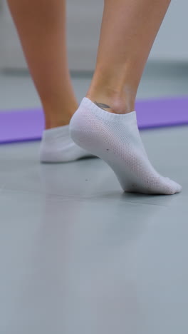 vista de la pierna trasera en calcetines equilibrándose en un pie con el talón elevado cerca del globo azul, alfombra púrpura en el suelo, entorno de gimnasio visible, capturando la estabilidad, entrenamiento de equilibrio en fitness